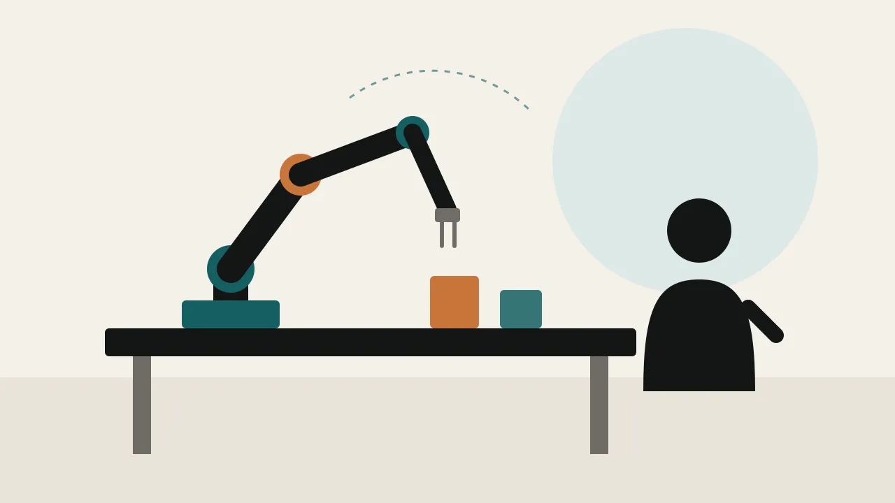A six axis robot arm on a workbench lifting a part while an operator stands nearby, seen from behind