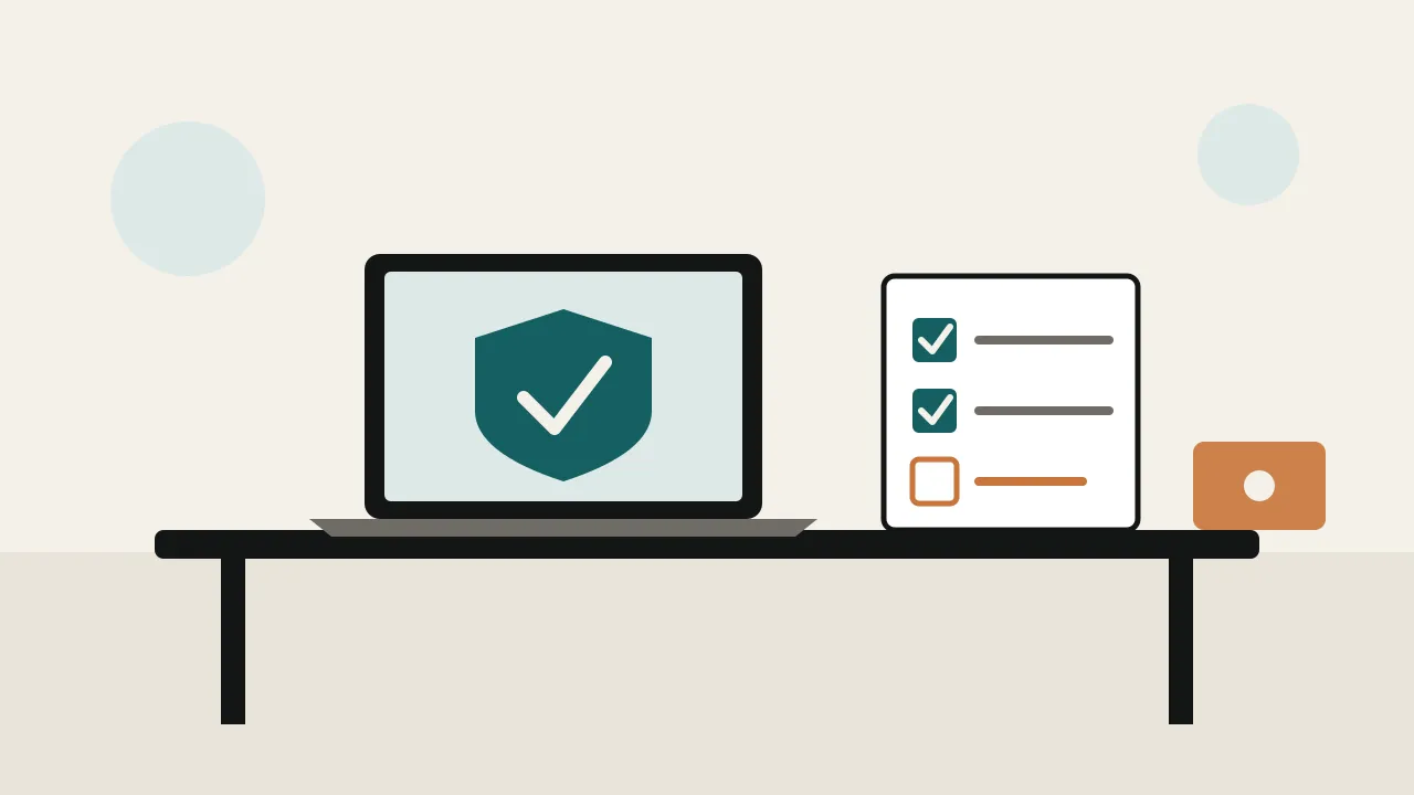 A laptop on an office desk beside a shield and a checklist with ticks, with a second small device set apart from the desk